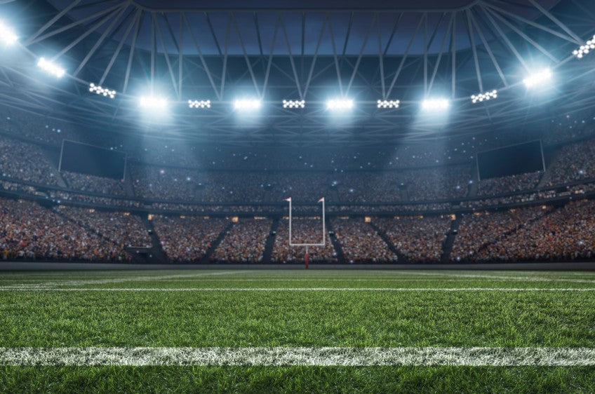 A football stadium shines bright with its lights at night time. The venue is packed with fans from top to bottom.