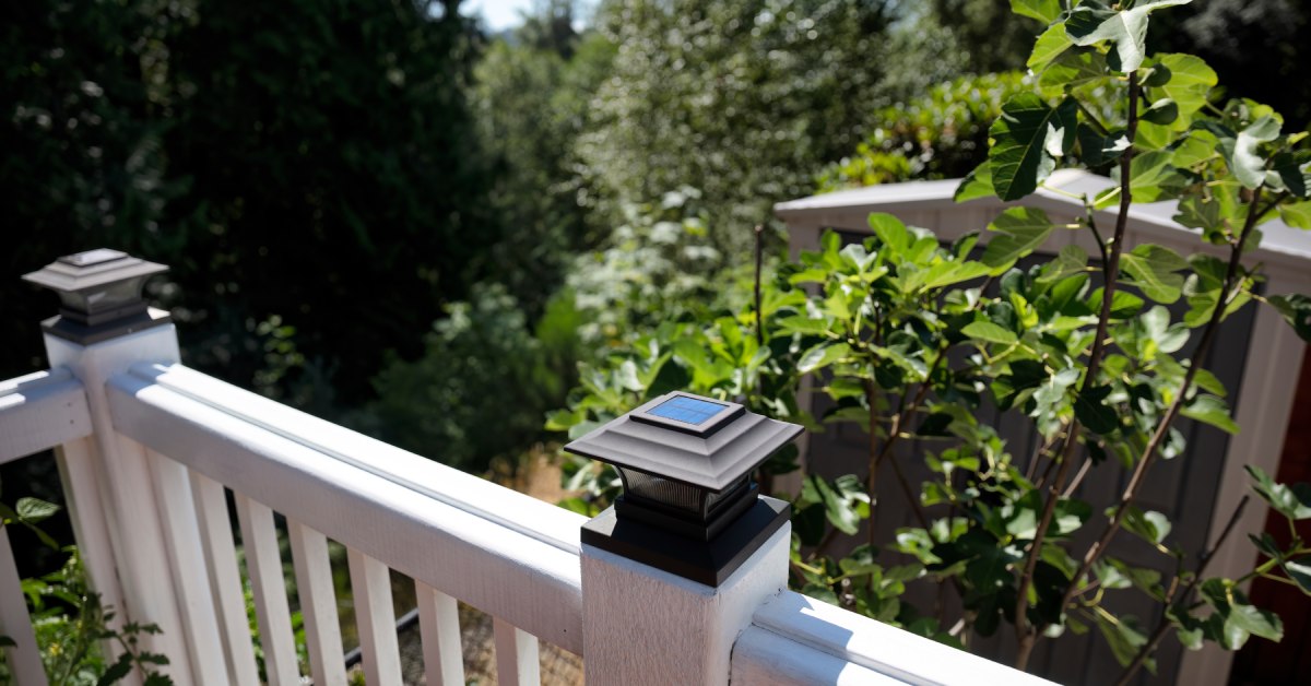 A home's outdoor railing, featuring solar lights on top of each post. A forest with many trees fills the background.