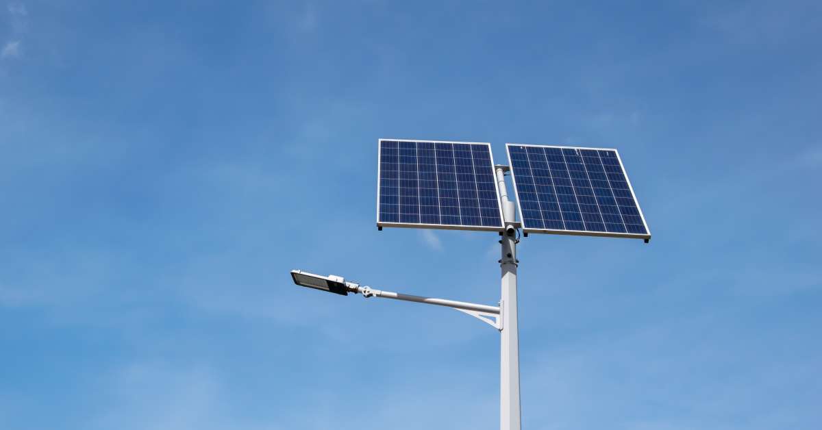 A solar street light stands during the daytime against a clear blue sky. It has two large blue solar panels.