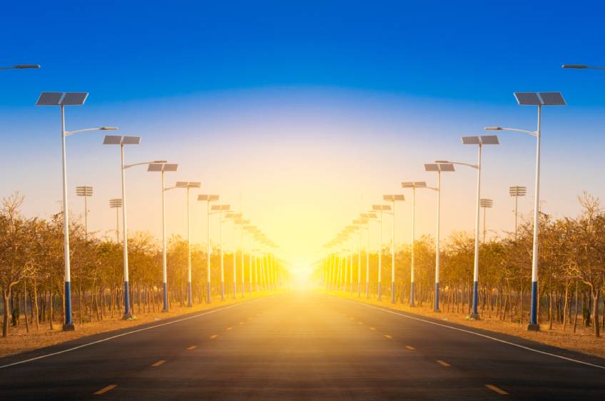 Rows of solar-powered street lights align the sides of a road while the sun goes down in the background.