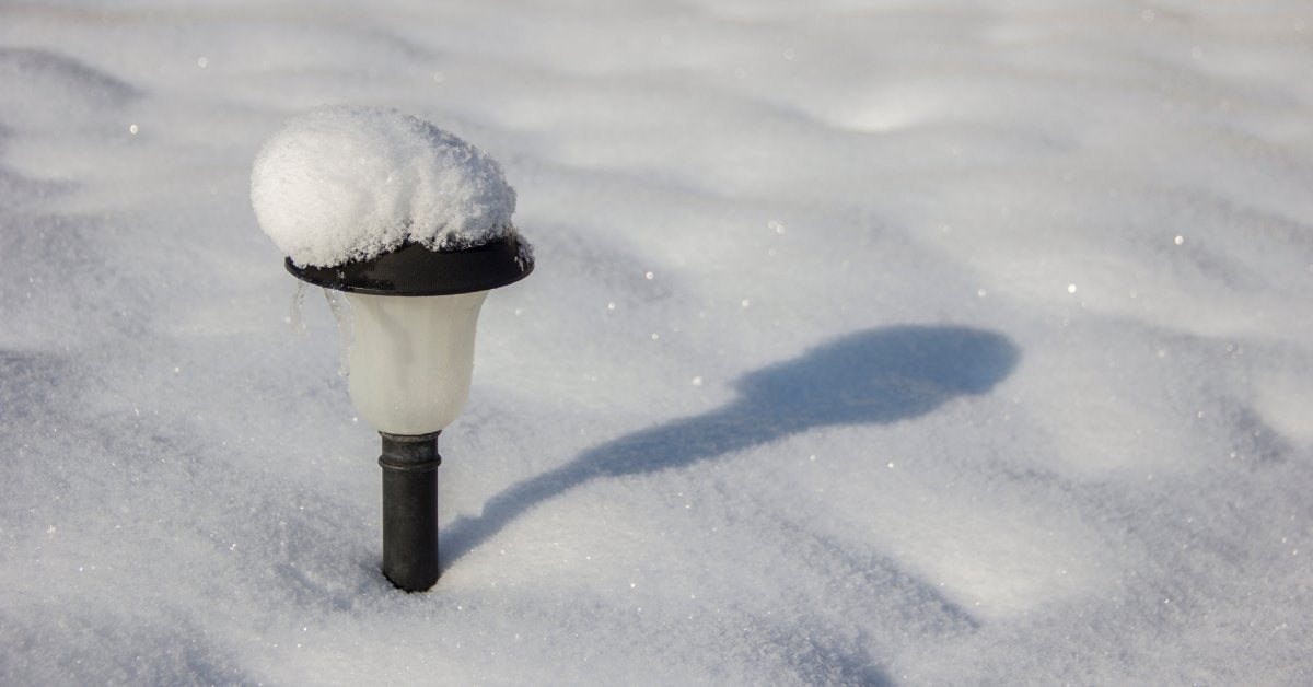 A solar garden light sits in the middle of a field of white snow. A small mound of snow sits on top of the light.